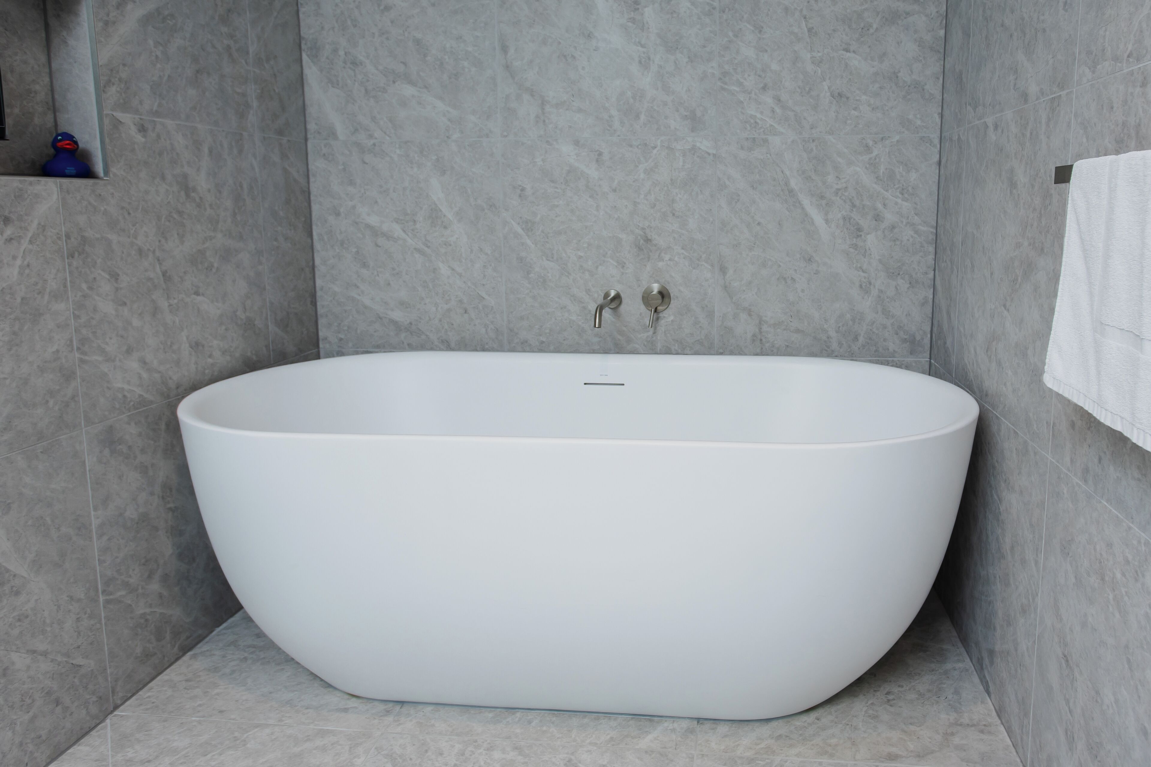 Un bagno moderno con una vasca da bagno indipendente, pareti in marmo e un porta asciugamani.