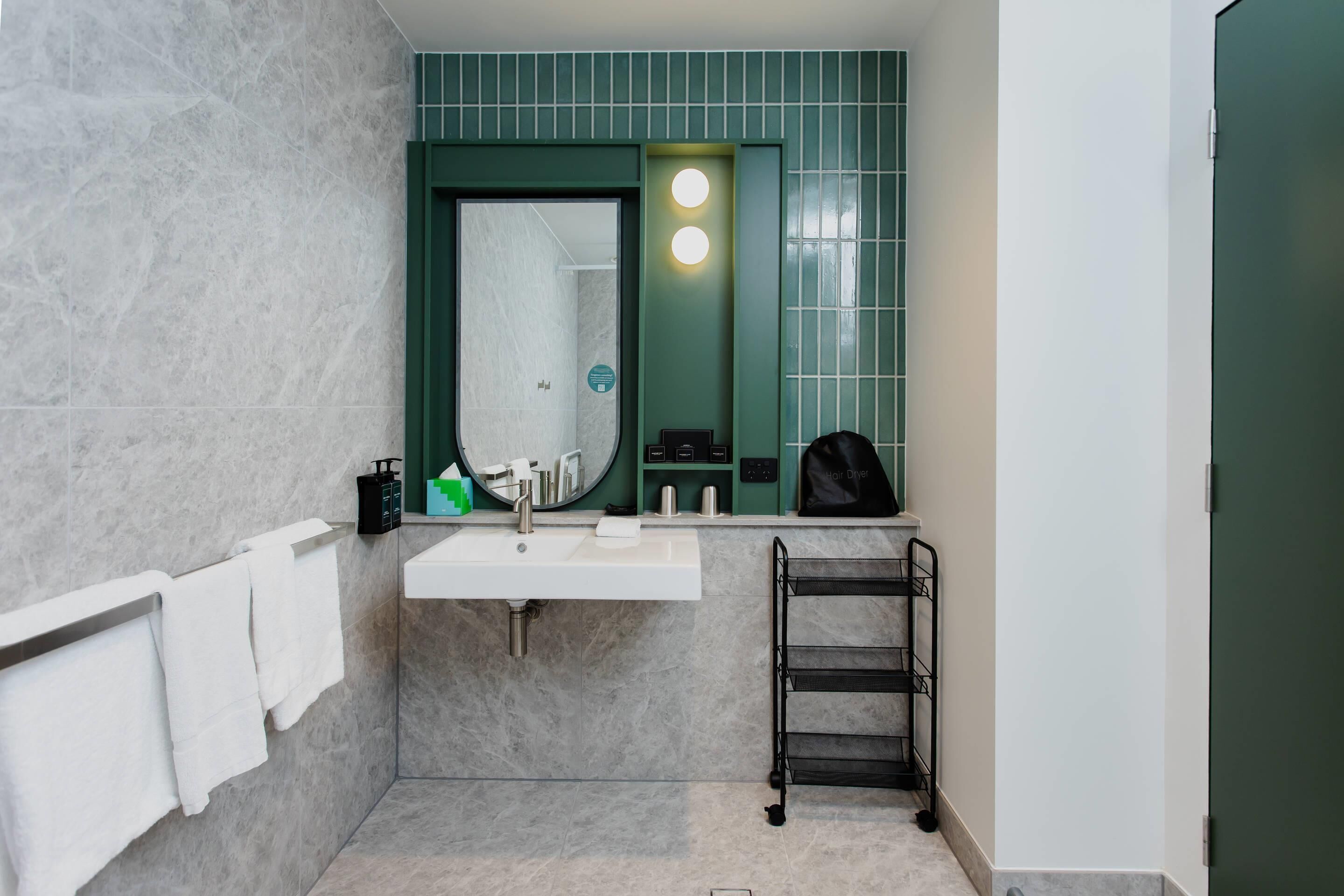 A bathroom with a white sink, green wall tiles, a towel rack, and a towel hanging on it.