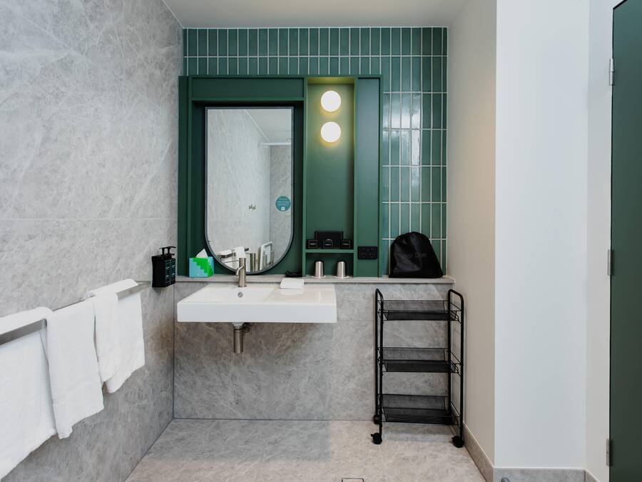 A bathroom with a white sink, green wall tiles, a towel rack, and a towel hanging on it.