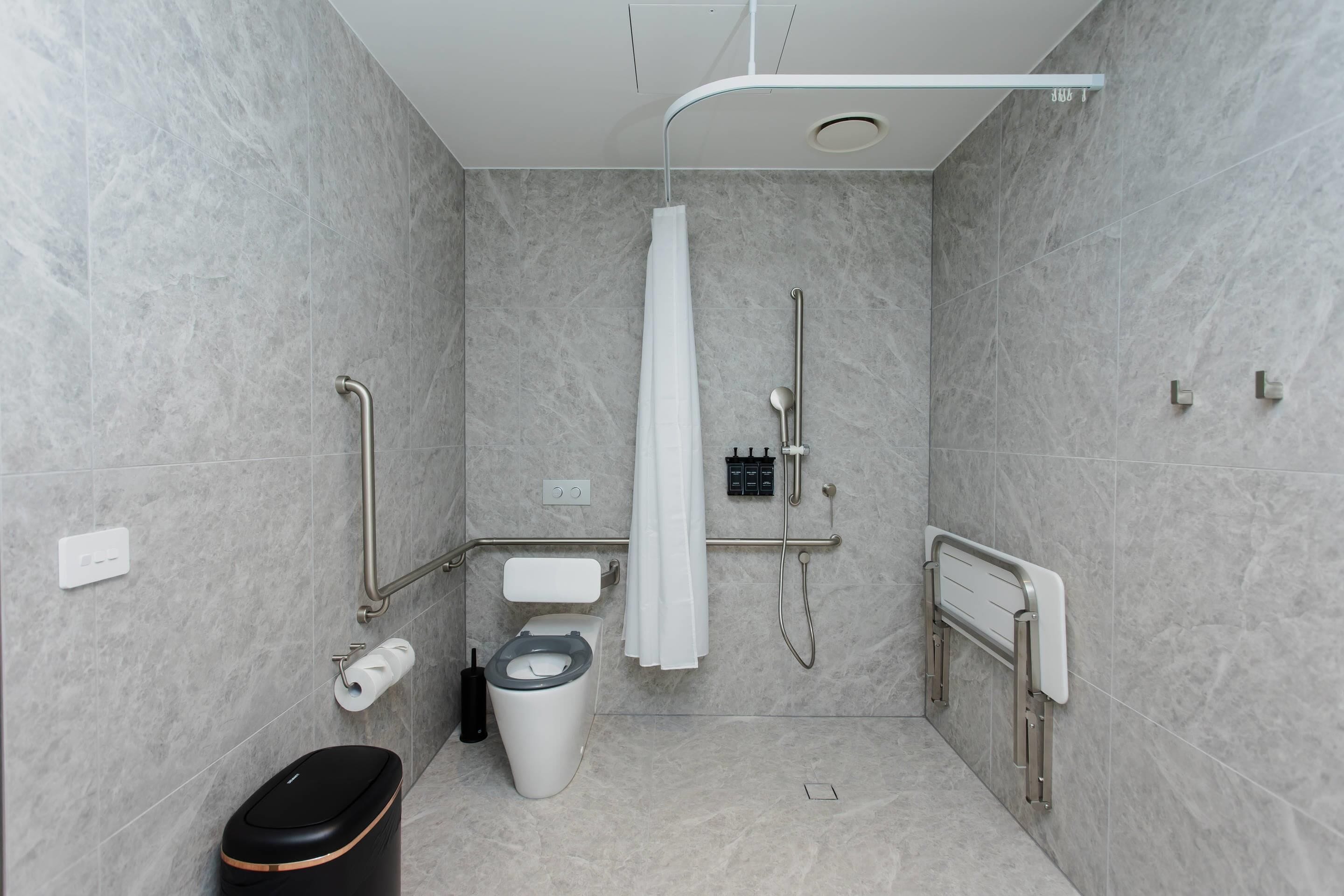 Un baño moderno con cabina de ducha, barras de apoyo, inodoro y cubo de basura.