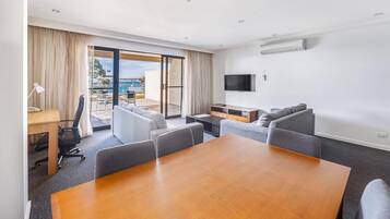 Habitación de hotel con una mesa de comedor, sillas, un sofá, un televisor y un balcón con vistas.