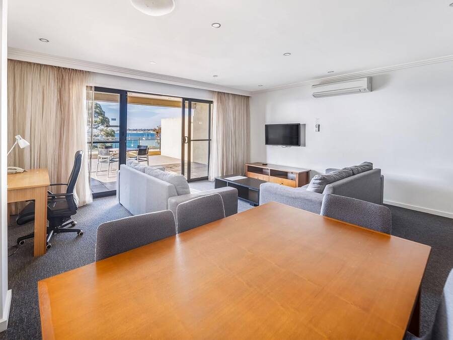 Habitación de hotel con una mesa de comedor, sillas, un sofá, un televisor y un balcón con vistas.