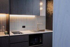 A modern kitchen with dark wood cabinets, a stainless steel sink, and a built-in microwave. - Bayside Geelong Hotel & Apartments, an Ascend Collection Hotel (Geelong)