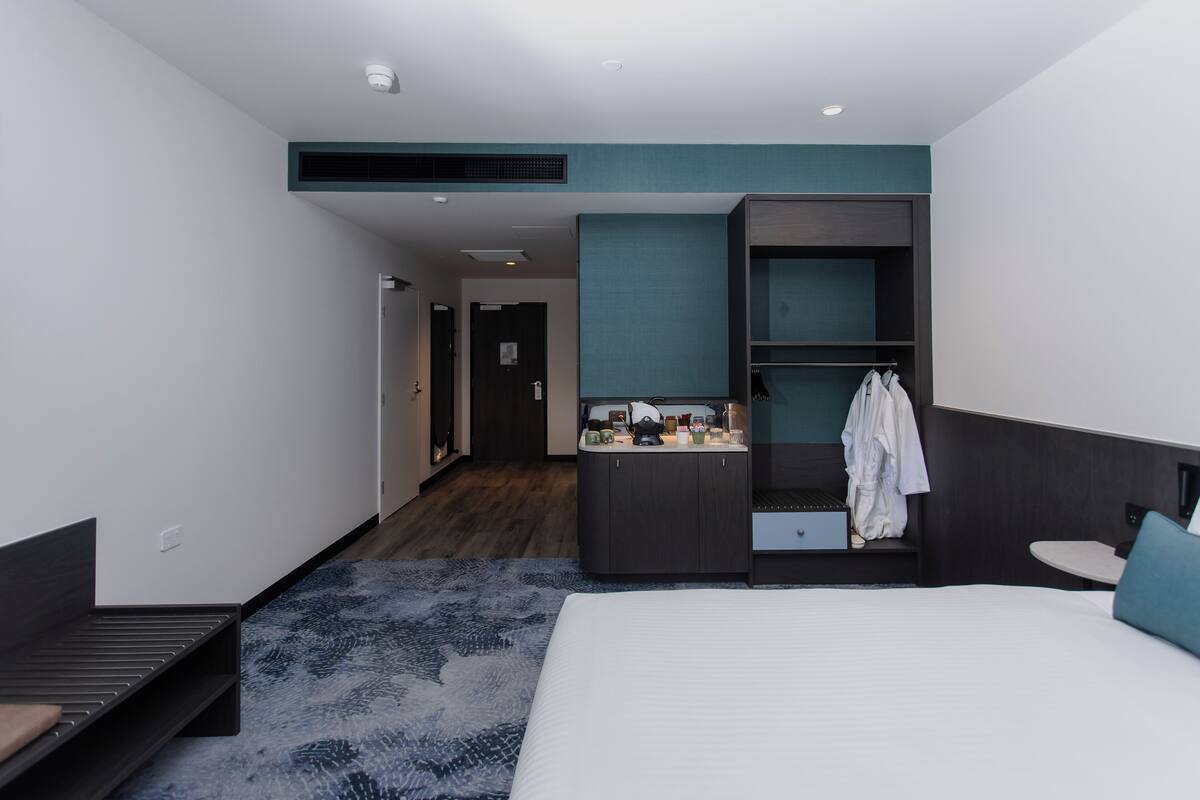 Een moderne hotelkamer met een groot bed, een klein bureau, een kaptafel met spiegel en een kledingkast.