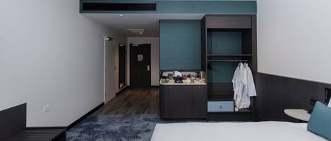 A modern hotel room with a large bed, a small desk, a vanity with a mirror, and a wardrobe.