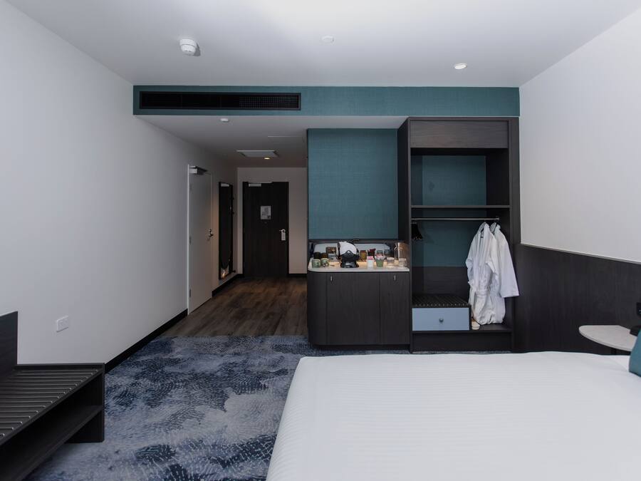 Habitació d'hotel moderna amb un llit gran, un escriptori petit, una tocador amb mirall i un armari.