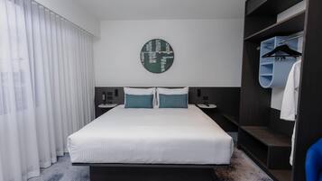 A modern hotel room with a large bed, a round wall clock, a wardrobe, and a mirror.