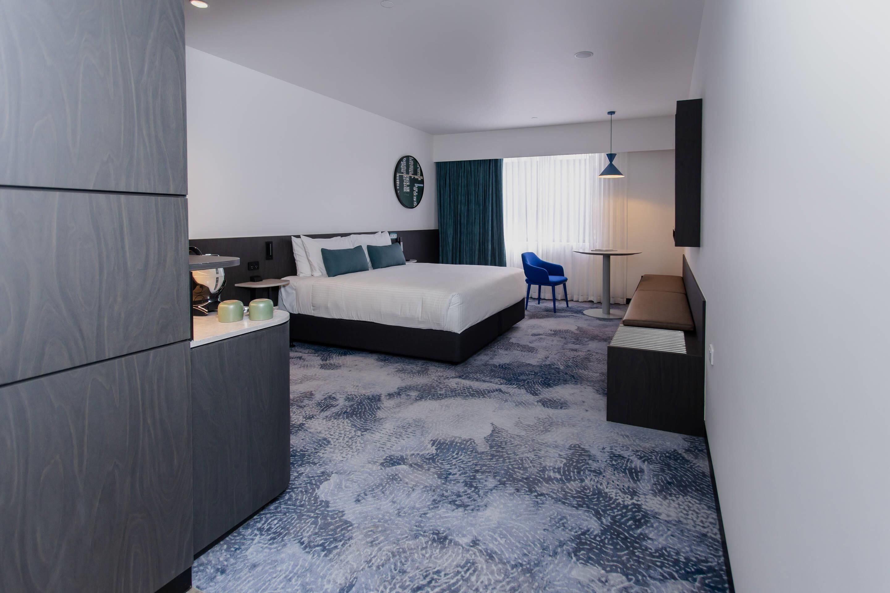 A modern hotel room with a bed, a desk, a chair, and a small table.