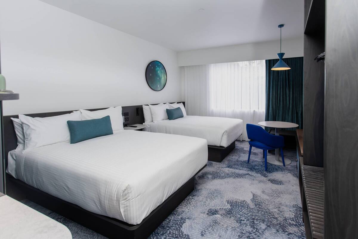 Een hotelkamer met twee bedden, een ronde wandklok, een blauwe stoel en een kleine tafel.