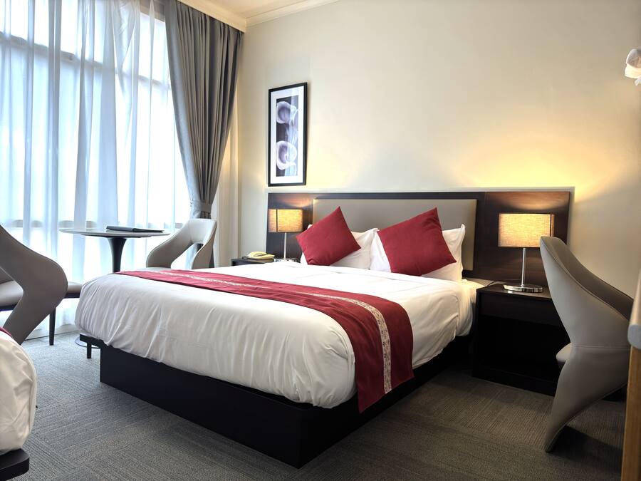 Une chambre d’hôtel comprenant un lit, deux tables de chevet, une chaise, un bureau, une lampe et une fenêtre avec des rideaux.