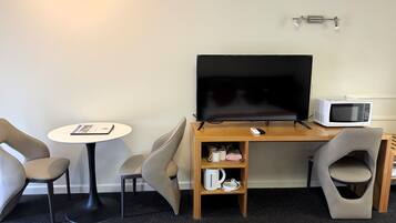 Une chambre d’hôtel équipée d’un bureau en bois, d’un téléviseur à écran plat, d’un four à micro-ondes, d’une télécommande et de deux chaises.