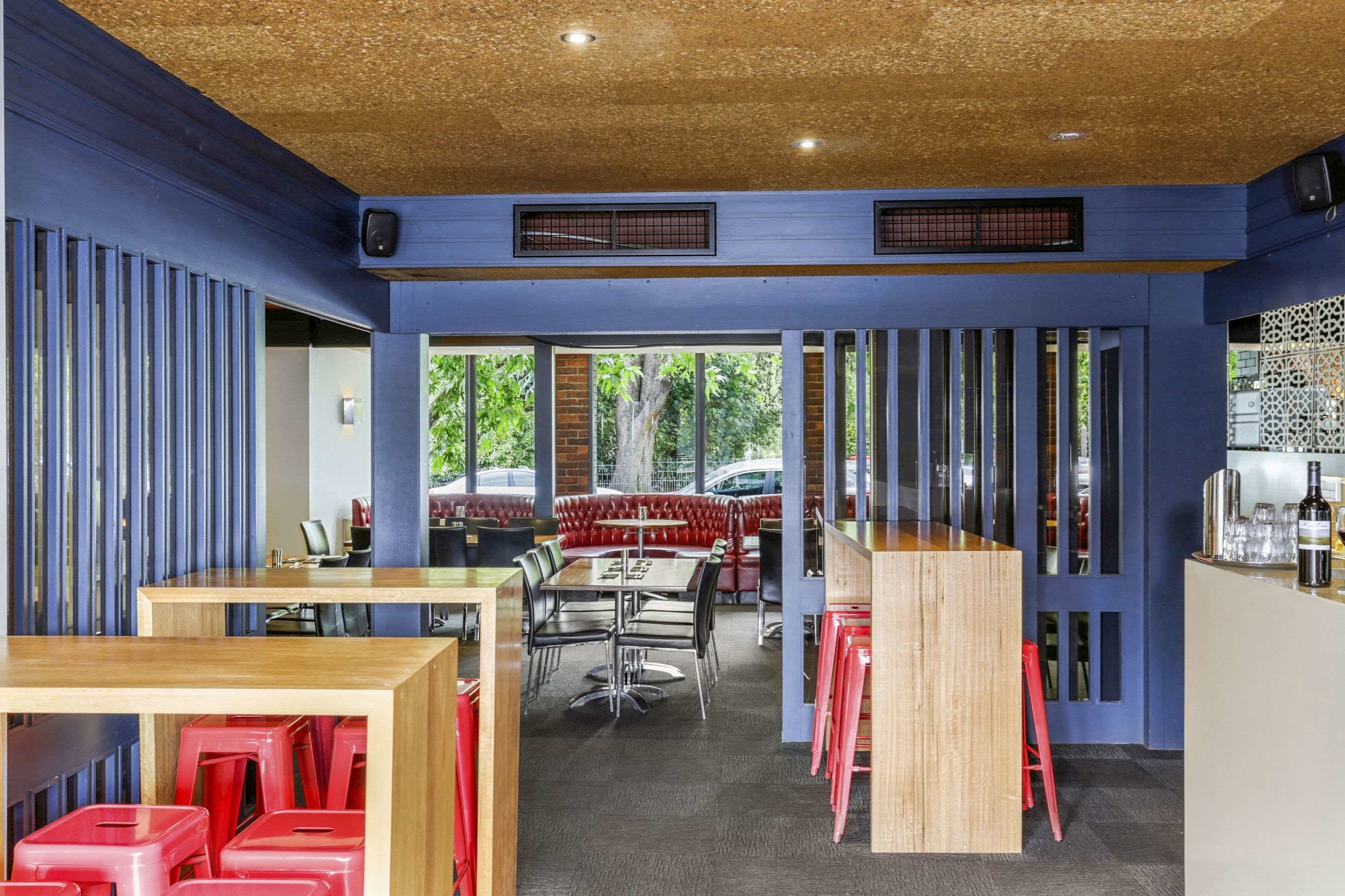 A restaurant with a modern interior, featuring wooden tables and red chairs, with a view of the outside.