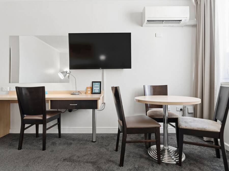 Ein Hotelzimmer mit Schreibtisch, zwei Stühlen, Fernseher und Klimaanlage.