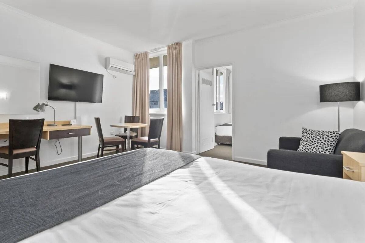 A hotel room with a bed, desk, chairs, a TV, and a sofa.