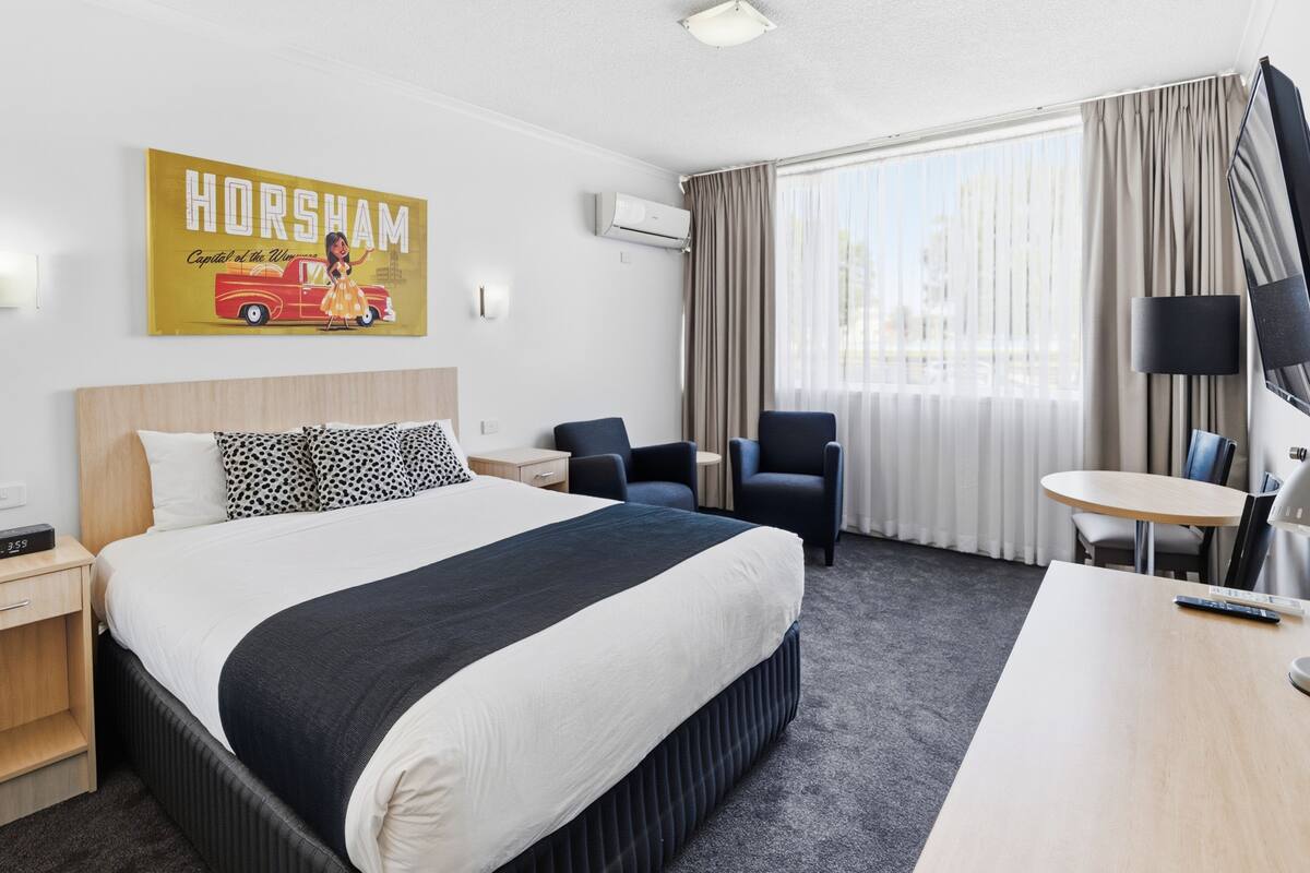 A hotel room with a bed, a desk, a chair, a TV, and a window with curtains.