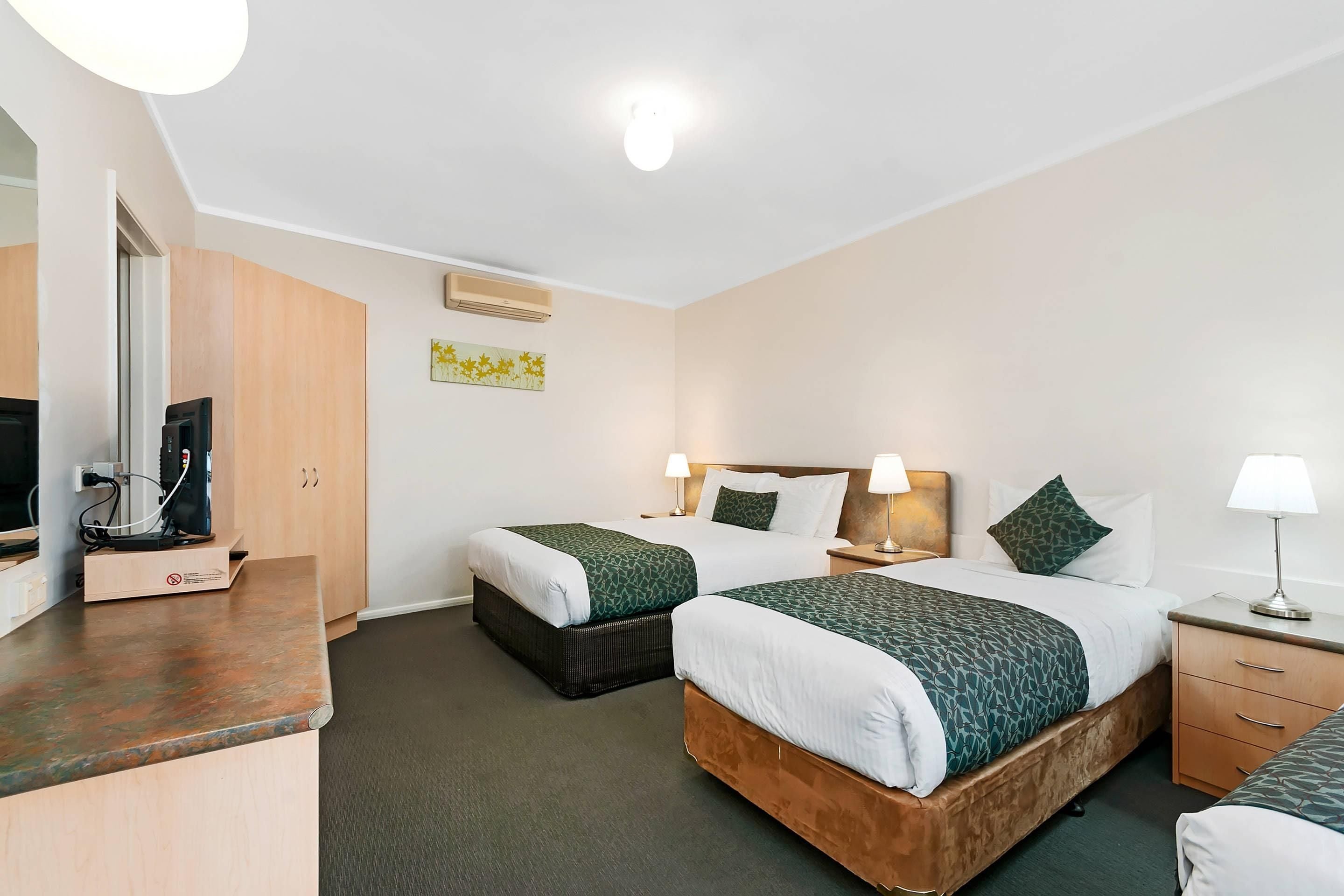 A hotel room with two beds, a desk with a coffee machine, a TV, and a mirror.