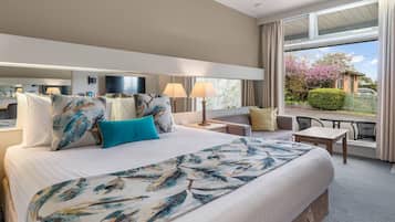A hotel room with a large bed, two bedside tables, a sitting area with a chair and a small table, and a balcony with a view of the outside.