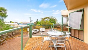 A balcony with a wooden deck, metal chairs, a table, and a view of a parking area and buildings in the distance. - Comfort Inn & Suites Lakes Entrance (Lakes Entrance)