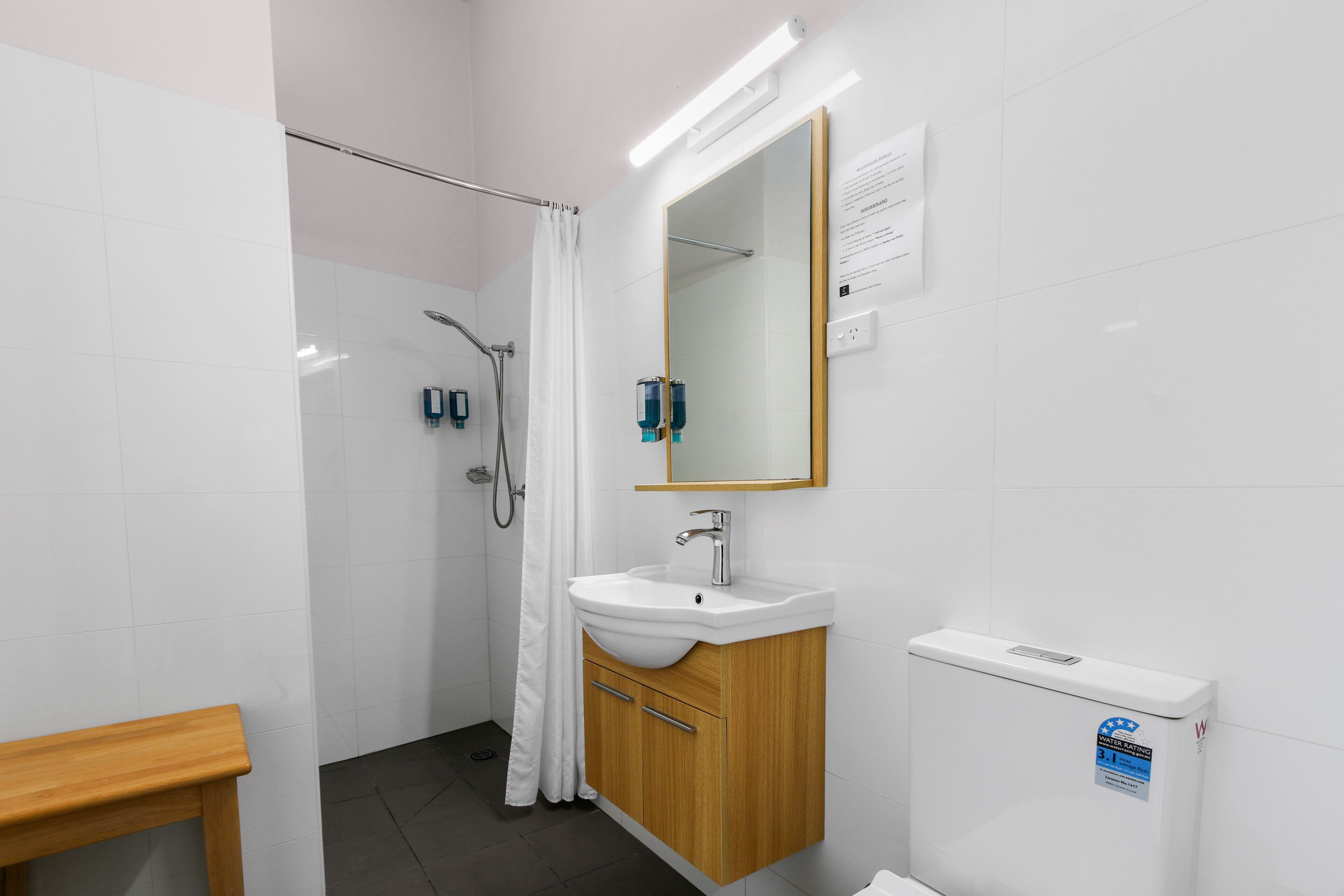 Ein modernes Badezimmer mit einem weißen Waschbecken, einem Holz-Waschtisch, einem großen Spiegel und einer Duschkabine.