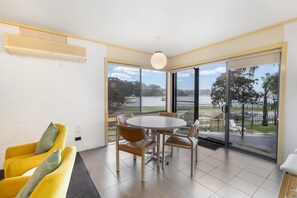 A modern room with a dining table and chairs, a yellow sofa, and large windows offering a view of a body of water and greenery. - Comfort Inn & Suites Lakes Entrance (Lakes Entrance)