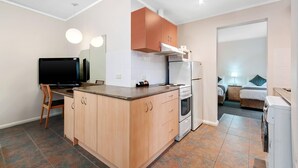 A compact kitchen with a TV, wooden cabinets, a stove, and a washing machine. - Comfort Inn & Suites Lakes Entrance (Lakes Entrance)