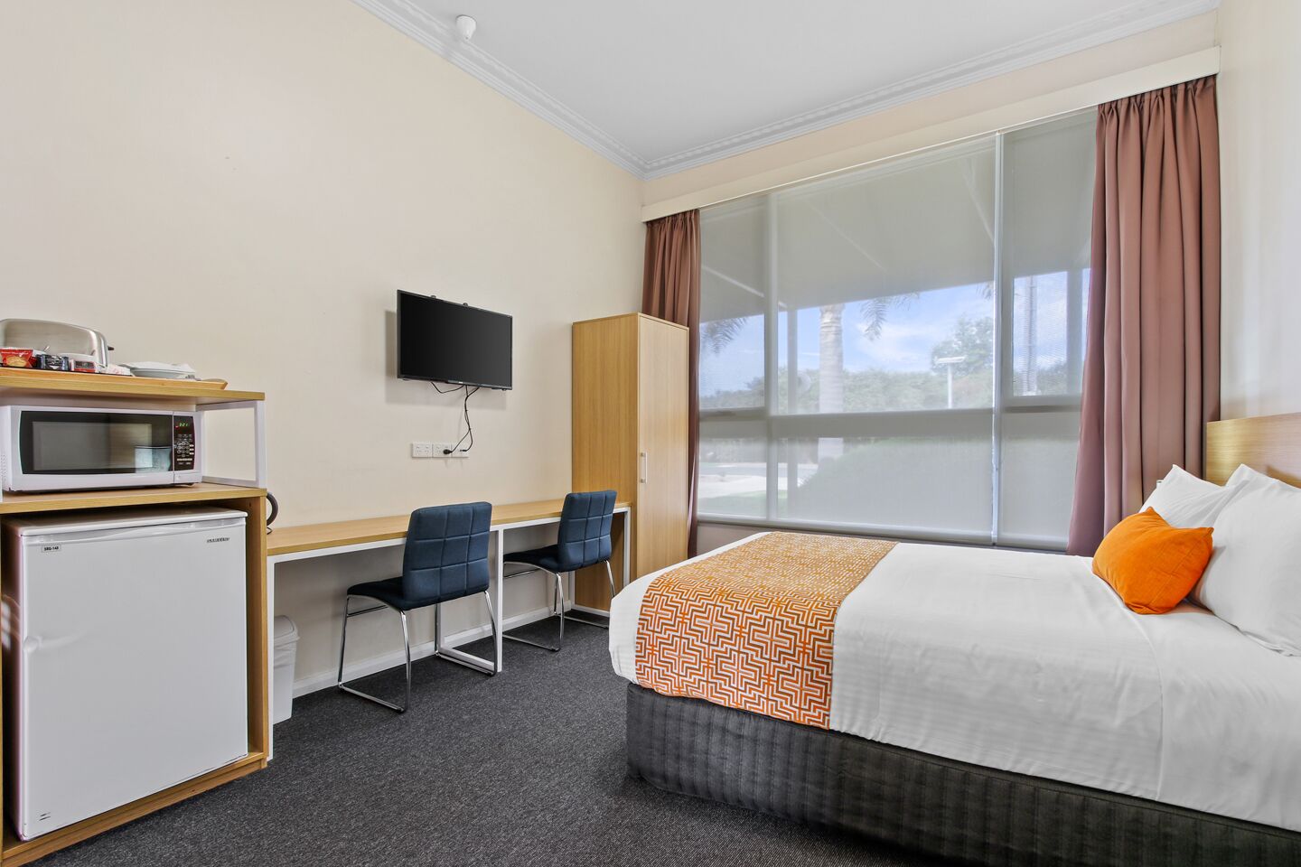 A hotel room with a bed, a desk with a computer, a microwave, and a television.