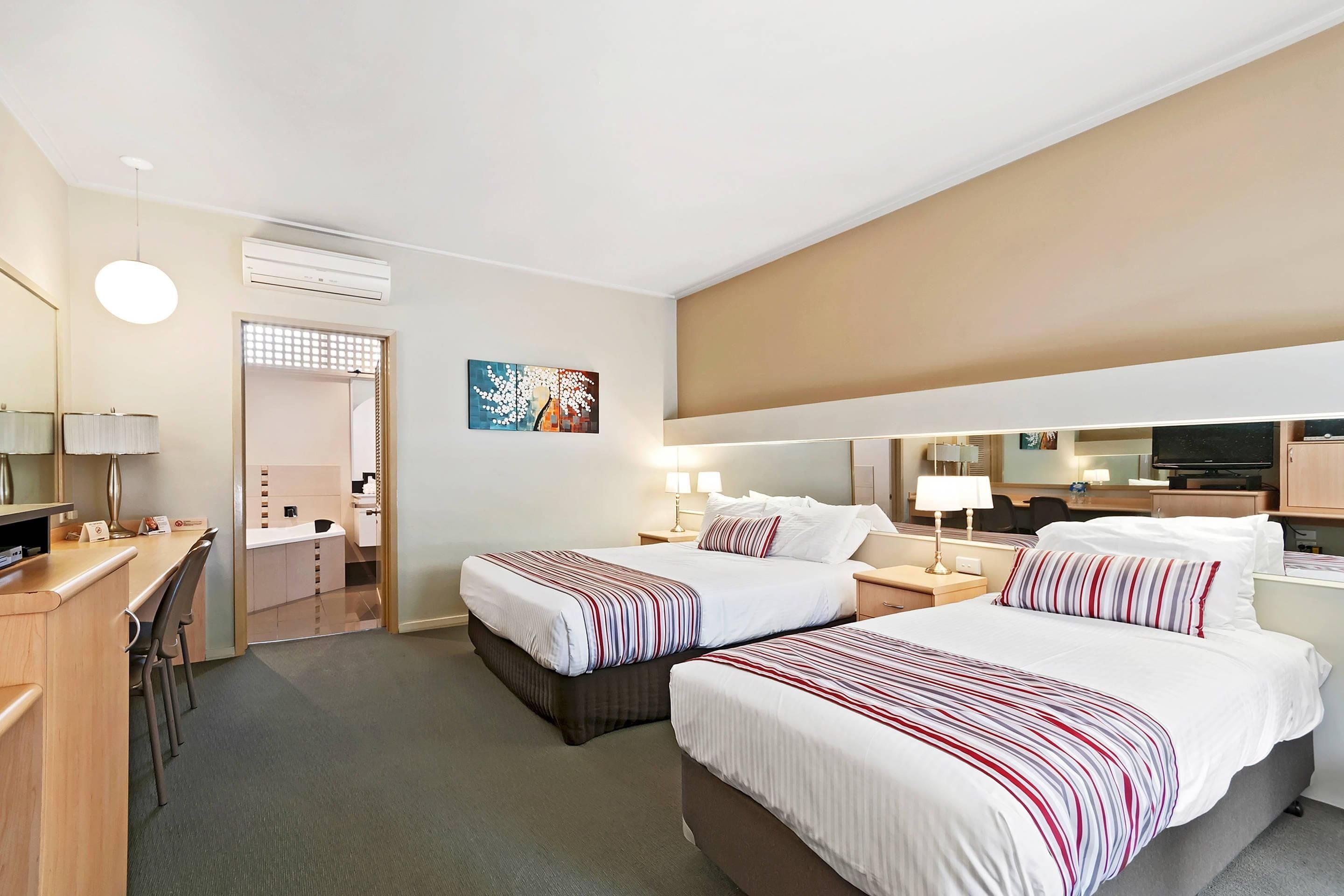 A hotel room with two beds, a desk, a chair, a TV, and a bathroom visible through an open door.