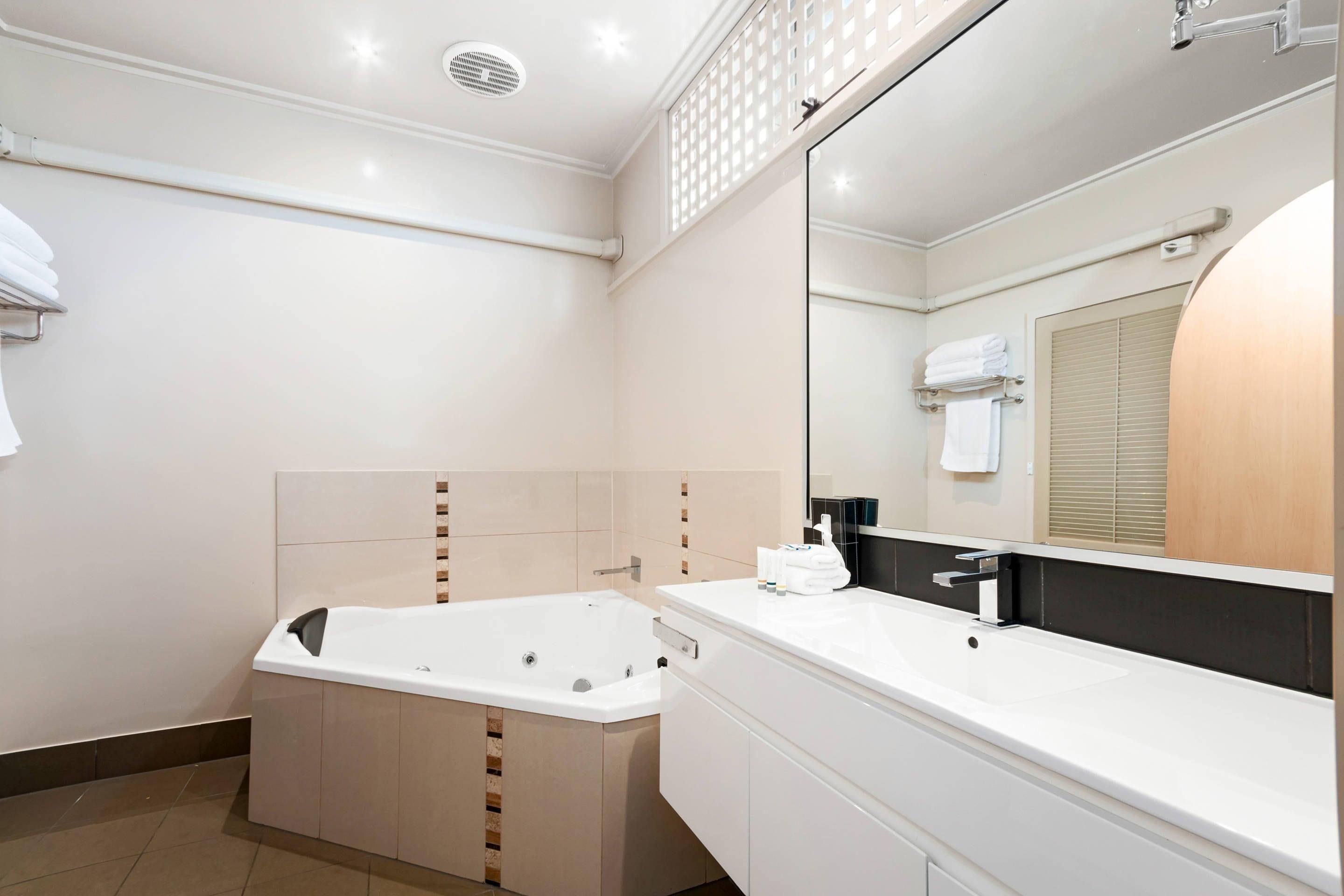 Un baño moderno con bañera, un espejo grande y un mueble de tocador blanco.