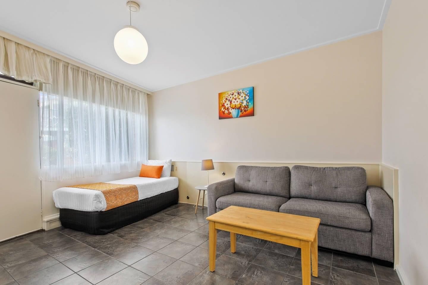 A room with a bed, a sofa, a table, a lamp, and a painting on the wall.