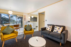 A modern living room with a sofa, two armchairs, a coffee table, and a dining area with a table and chairs. - Comfort Inn & Suites Lakes Entrance (Lakes Entrance)