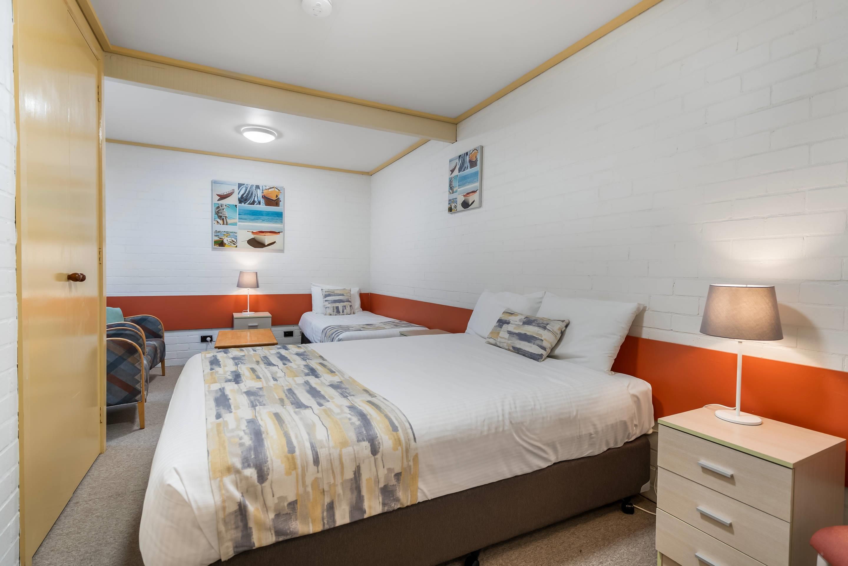 A bedroom with a bed, bedside tables, a lamp, a chair, and a wall with pictures.