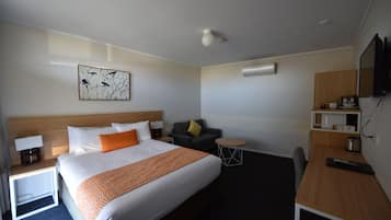 A hotel room with a large bed, a desk, a chair, a small table, a sofa, and a TV.