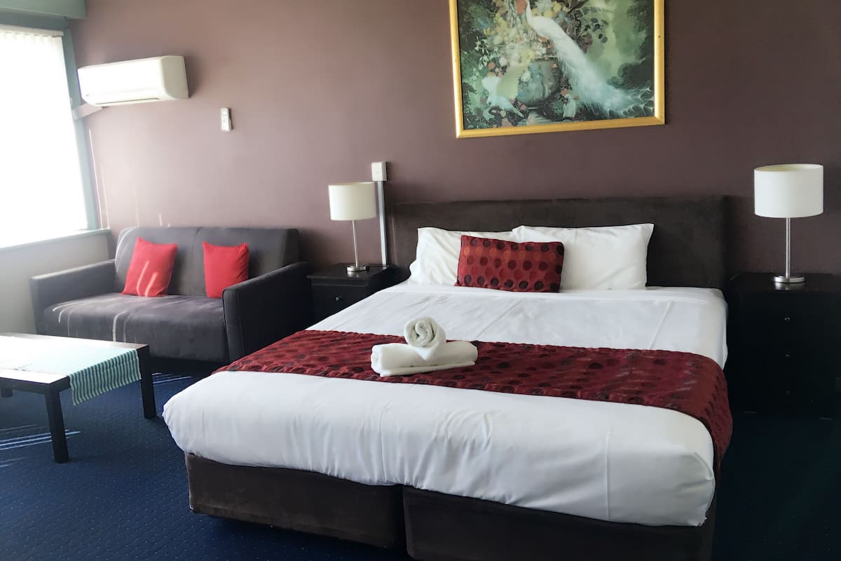 A hotel room with a large bed, a sofa, two nightstands, a painting, and a window.