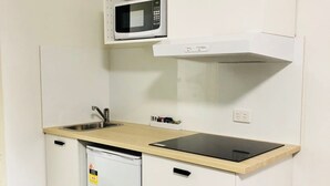 Una kitchenette compacta con microondas, lavamanos y un refrigerador pequeño.