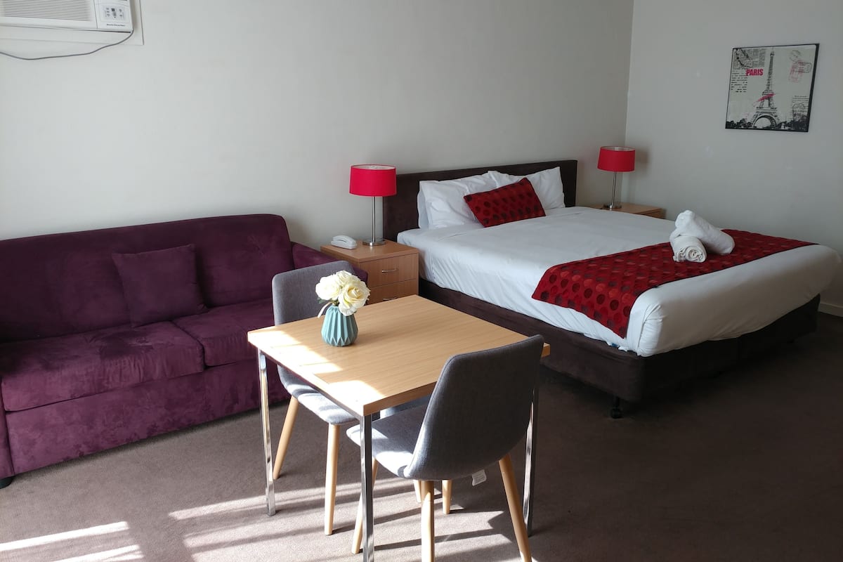 A hotel room with a bed, a desk, a chair, a couch, and a wall-mounted air conditioner.