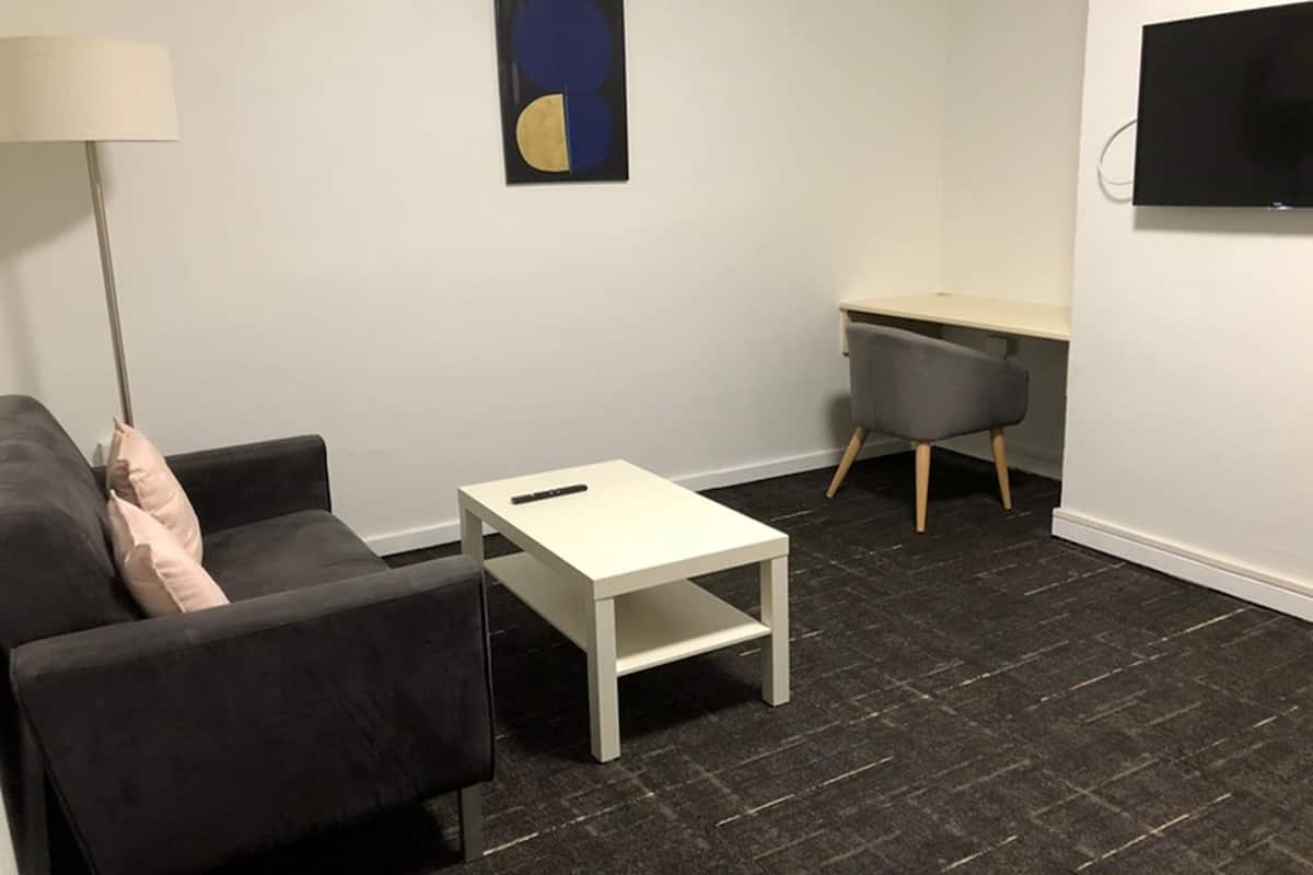 A modern living room with a sofa, a small white table, a desk, and a chair.
