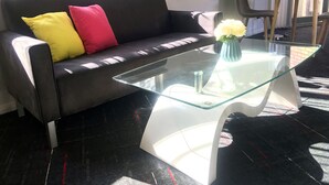 Una sala de estar moderna con un sofá de cuero negro, una mesa de centro de vidrio y un cojín amarillo y rojo.