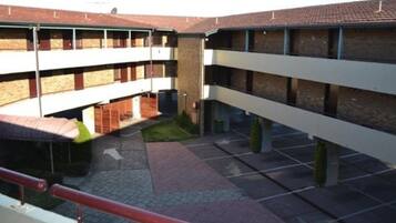 Un edificio de varios pisos con un patio. Varias balconadas con barandillas, un área de estar cubierta y un sendero pavimentado.