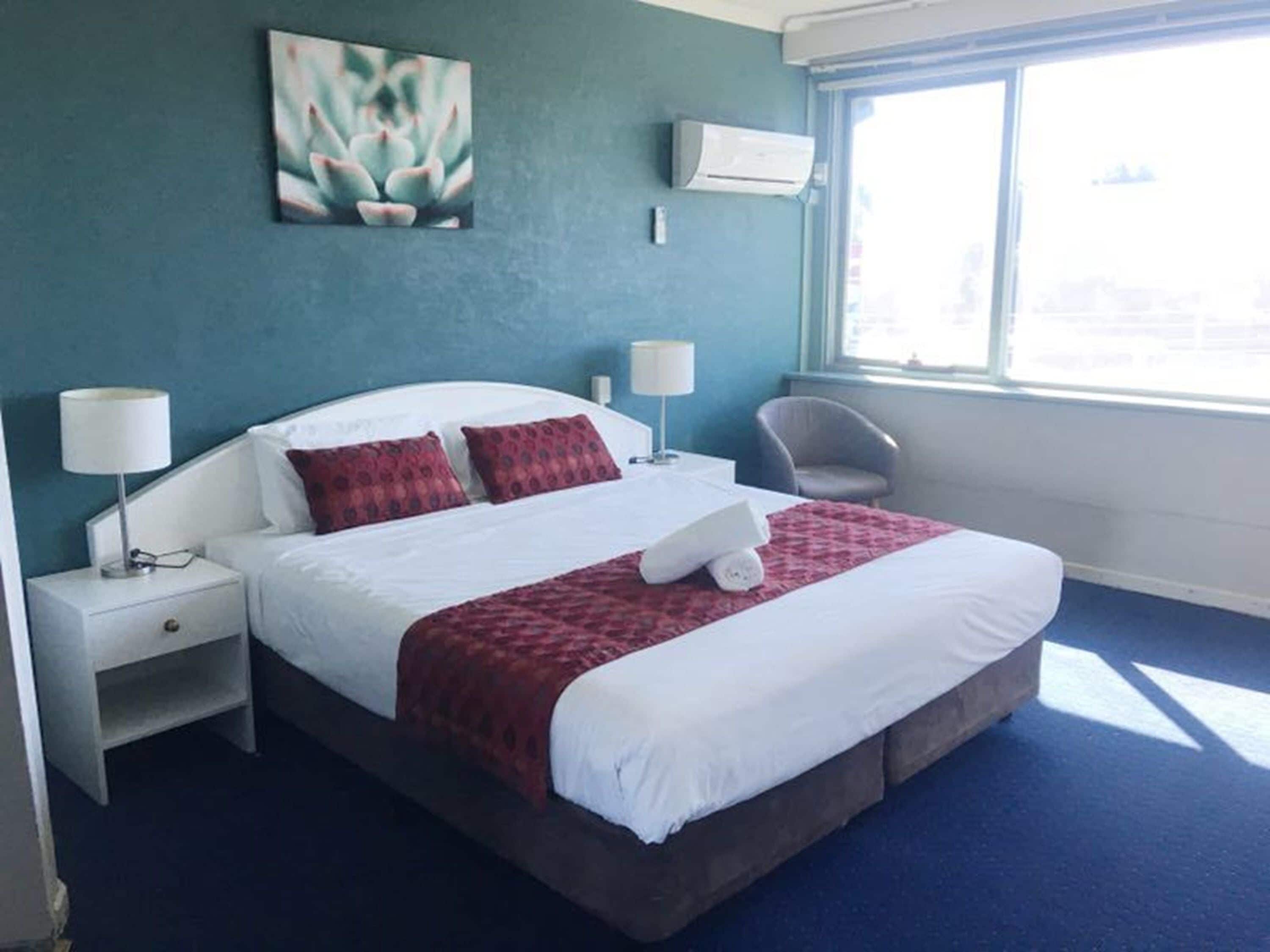 Una habitación de hotel con una cama, dos mesitas de noche, una silla y una ventana.