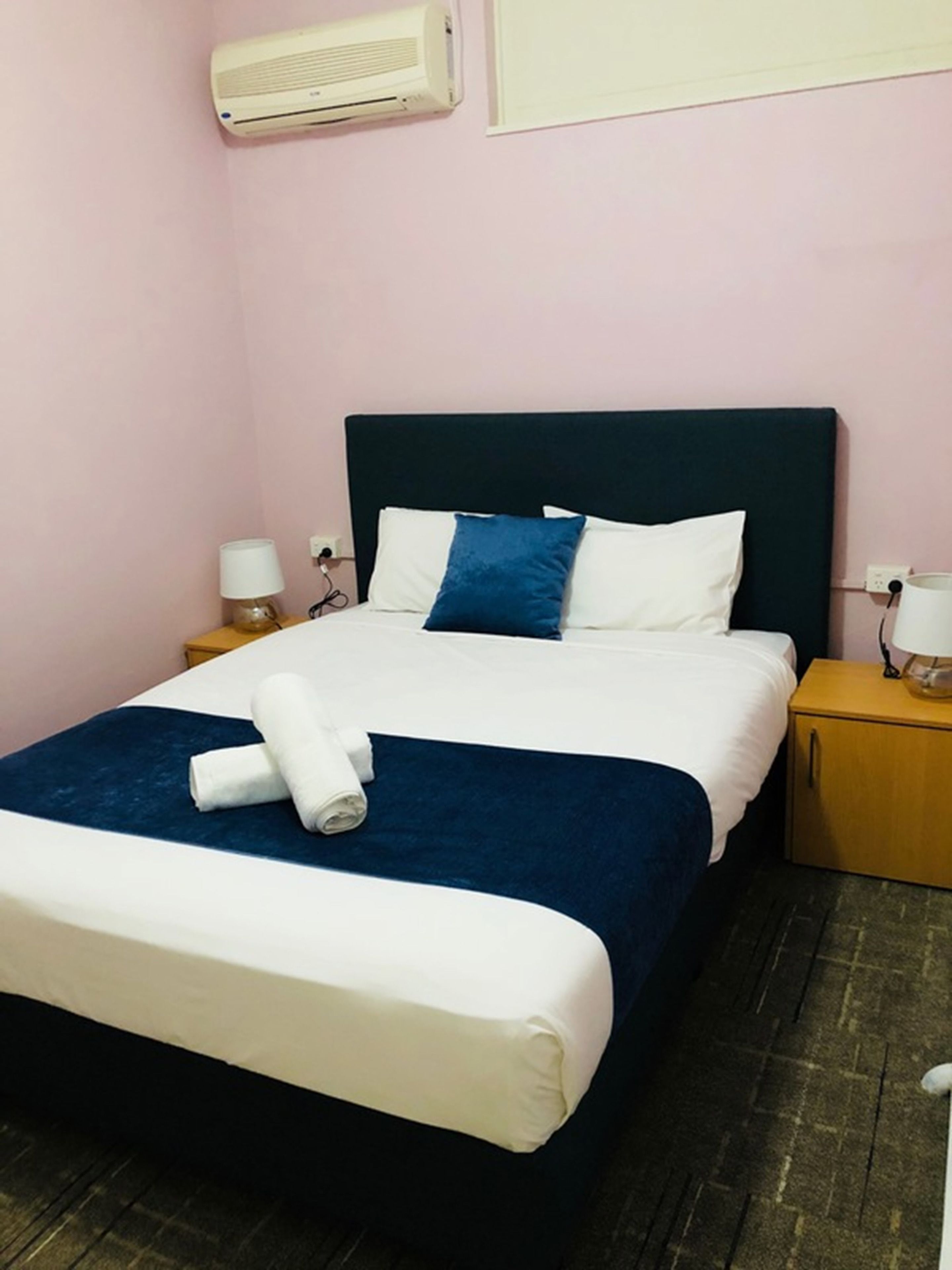 A neatly made bed with white and blue bedding, a dark headboard, and a folded towel on the footboard.