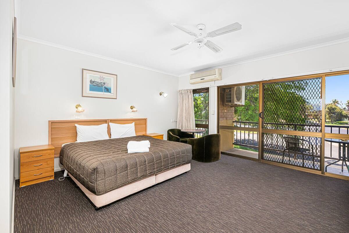 Une chambre d’hôtel avec un lit, un ventilateur de plafond, une fenêtre donnant sur un beau paysage et un balcon équipé de mobilier d’extérieur.