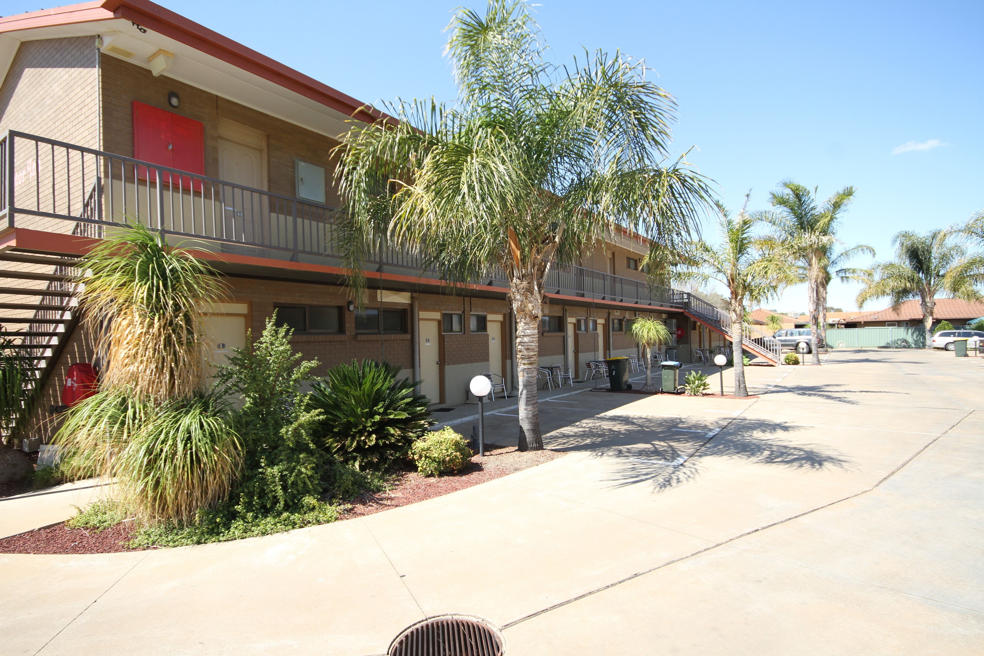 A two-story hotel with a red door, a balcony, and palm trees in the courtyard.
