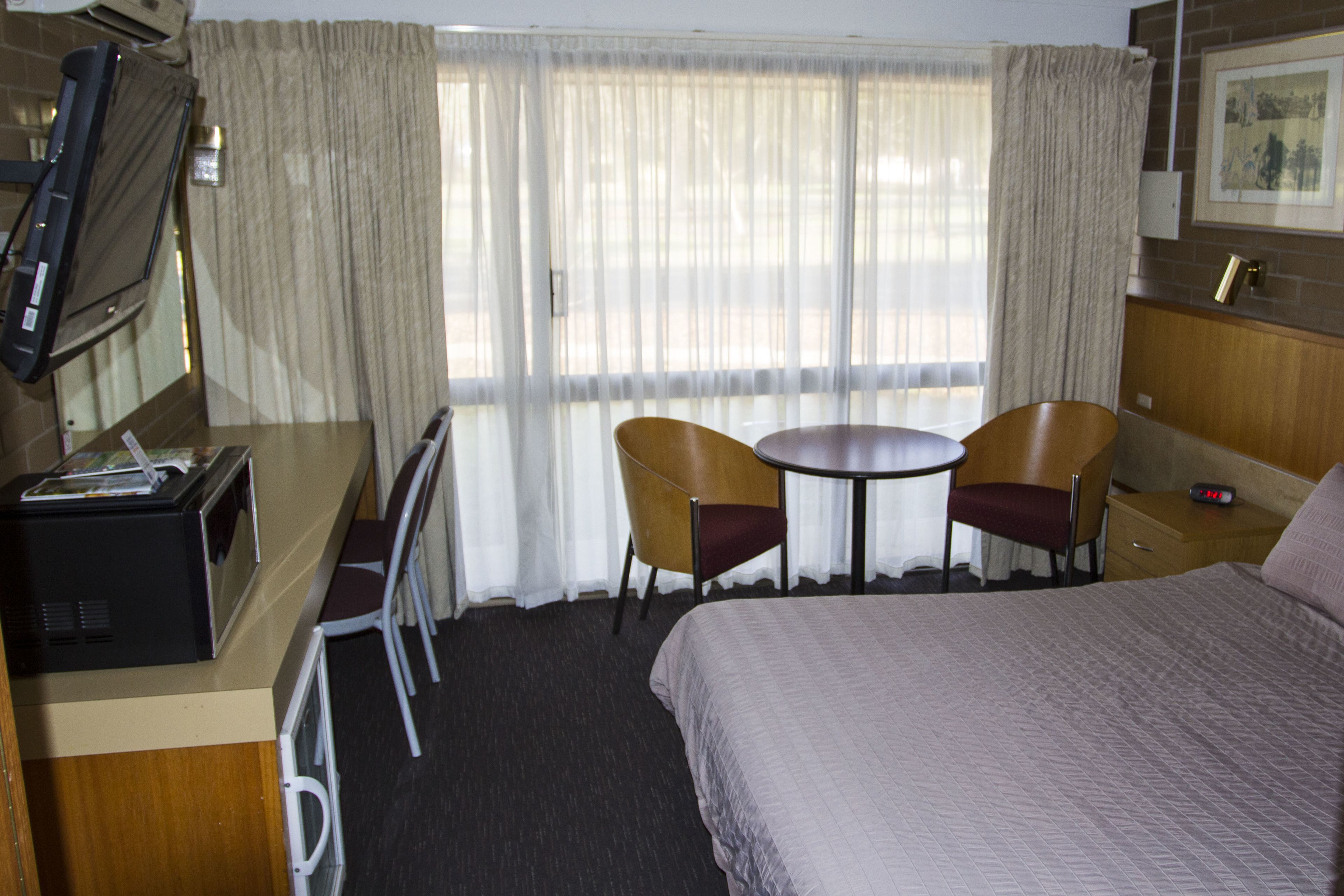 Habitación de hotel con cama, dos sillas, una mesita, televisor y ventana con cortinas.