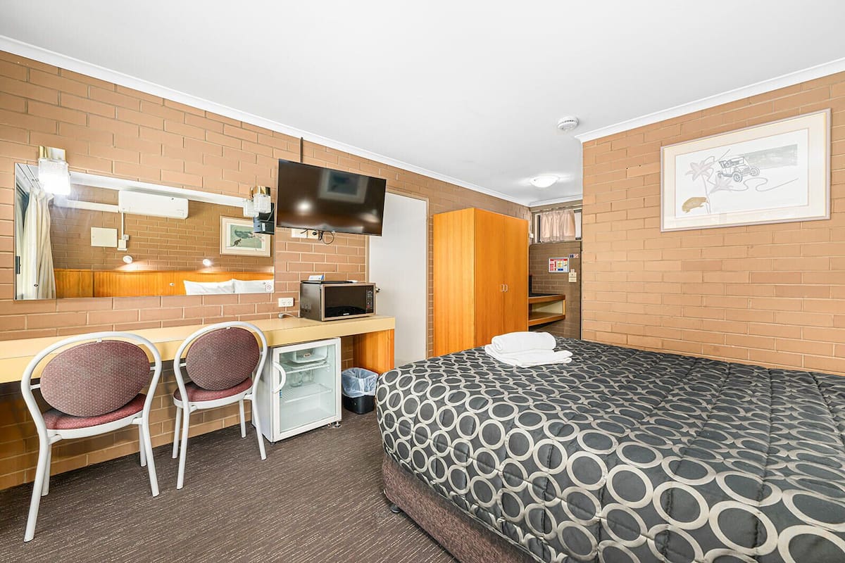 Une chambre d’hôtel comprenant un lit, un bureau avec deux chaises, une télévision, un four à micro-ondes et une armoire.