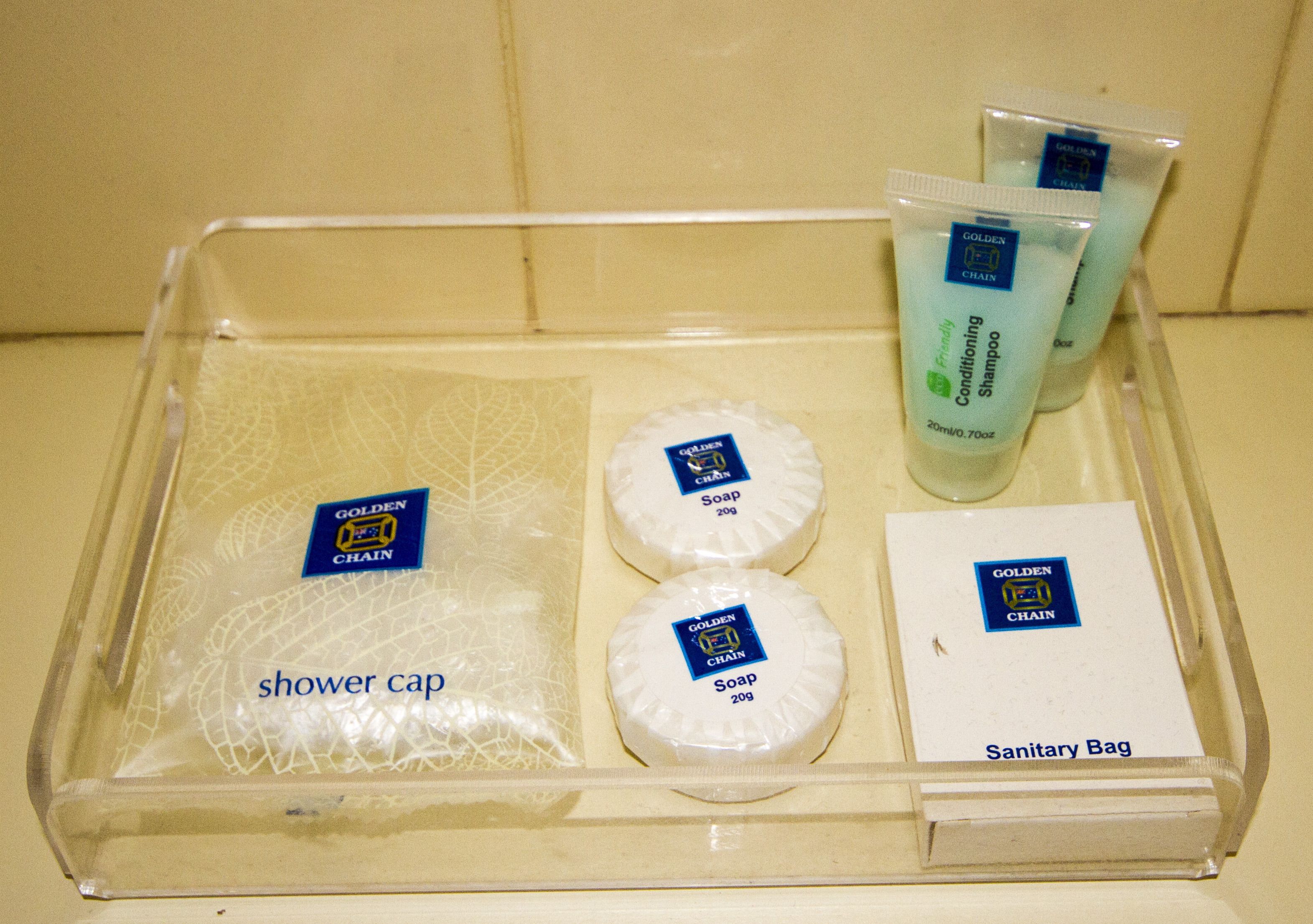 Un plateau en plastique transparent contenant un bonnet de douche, deux savons, un sac hygiénique et un tube de savon liquide.