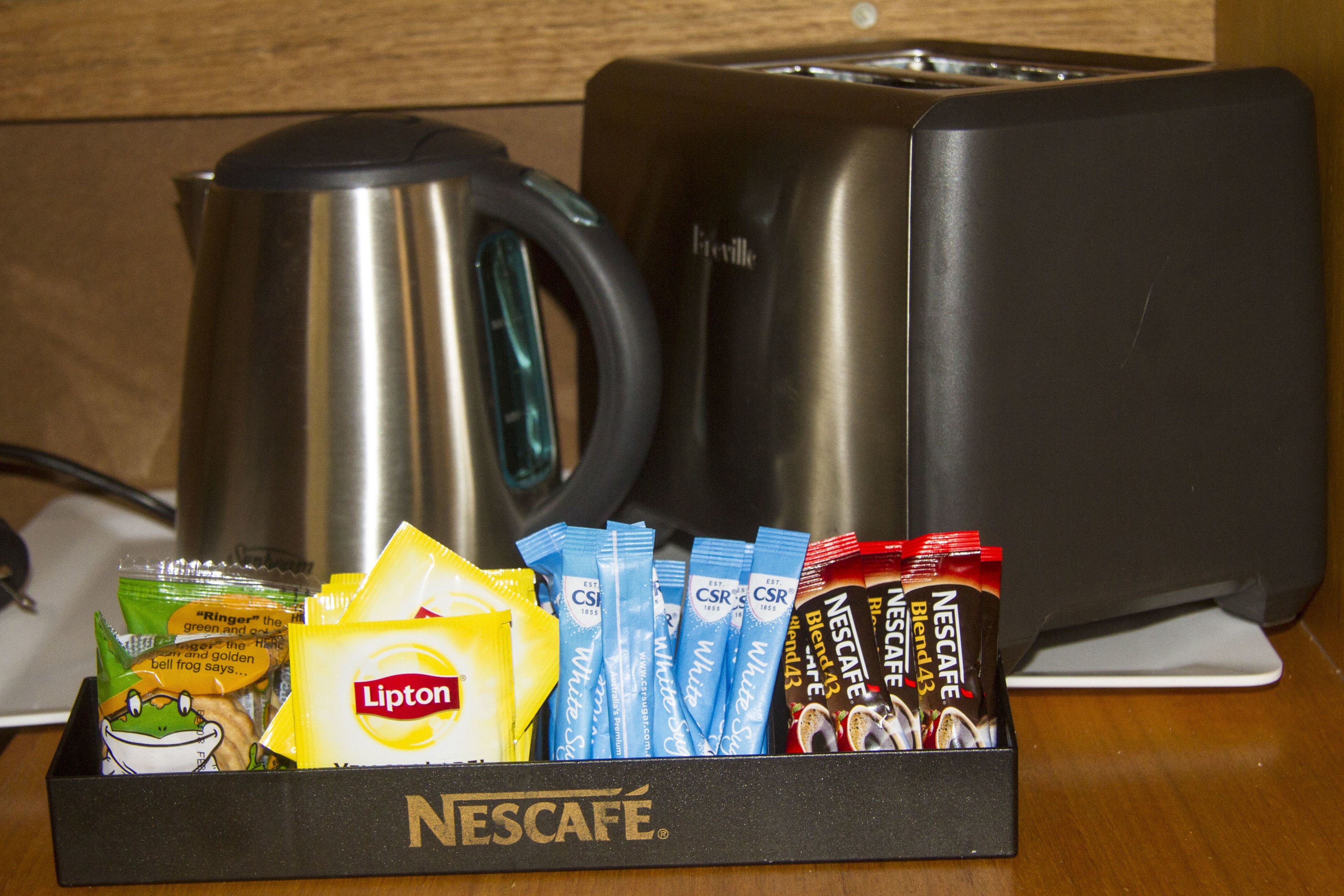 Uma bandeja com cápsulas de café Nescafé, saquinhos de chá Lipton e uma chaleira.