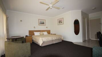 Quarto de hotel com cama, escrivaninha, cadeira, ventoinha no teto e duas imagens emolduradas na parede.