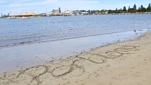 A beach with the word "Porto" written in the sand, boats in the water, and a distant cityscape.