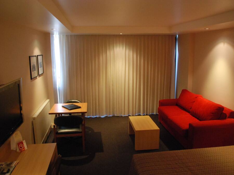 A hotel room with a red sofa, a wooden table, a TV, and a window with curtains.