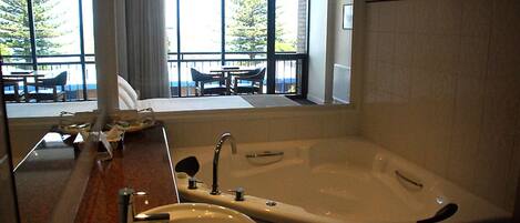 A bathroom with a bathtub, sink, and large windows overlooking a balcony with outdoor furniture.